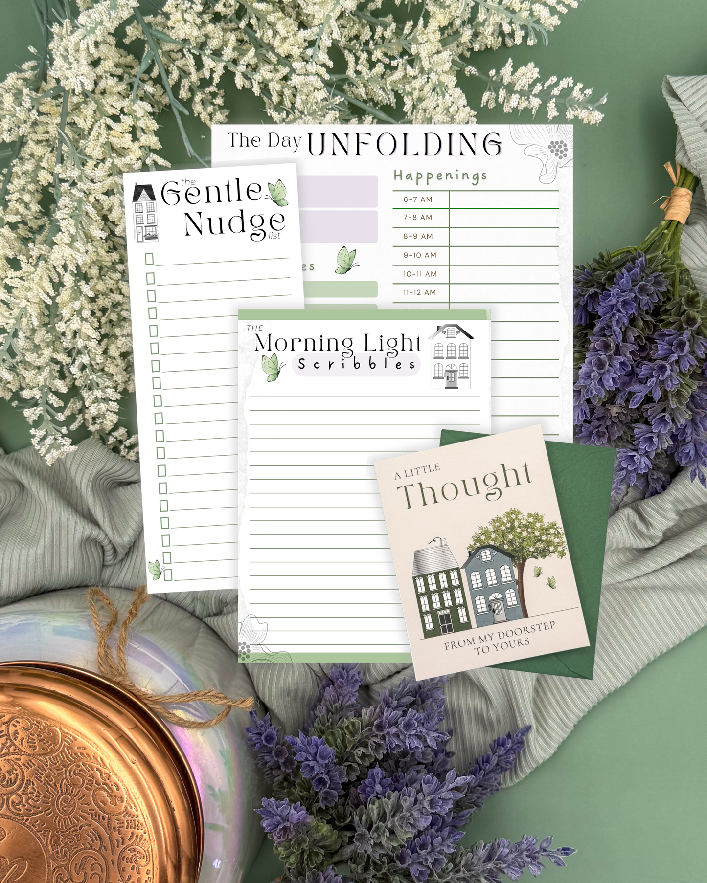 Collection of stationery items including a planner, postcard, and notepad on a green surface with flowers.