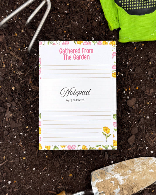 Notepad with floral design on garden soil with gardening tools