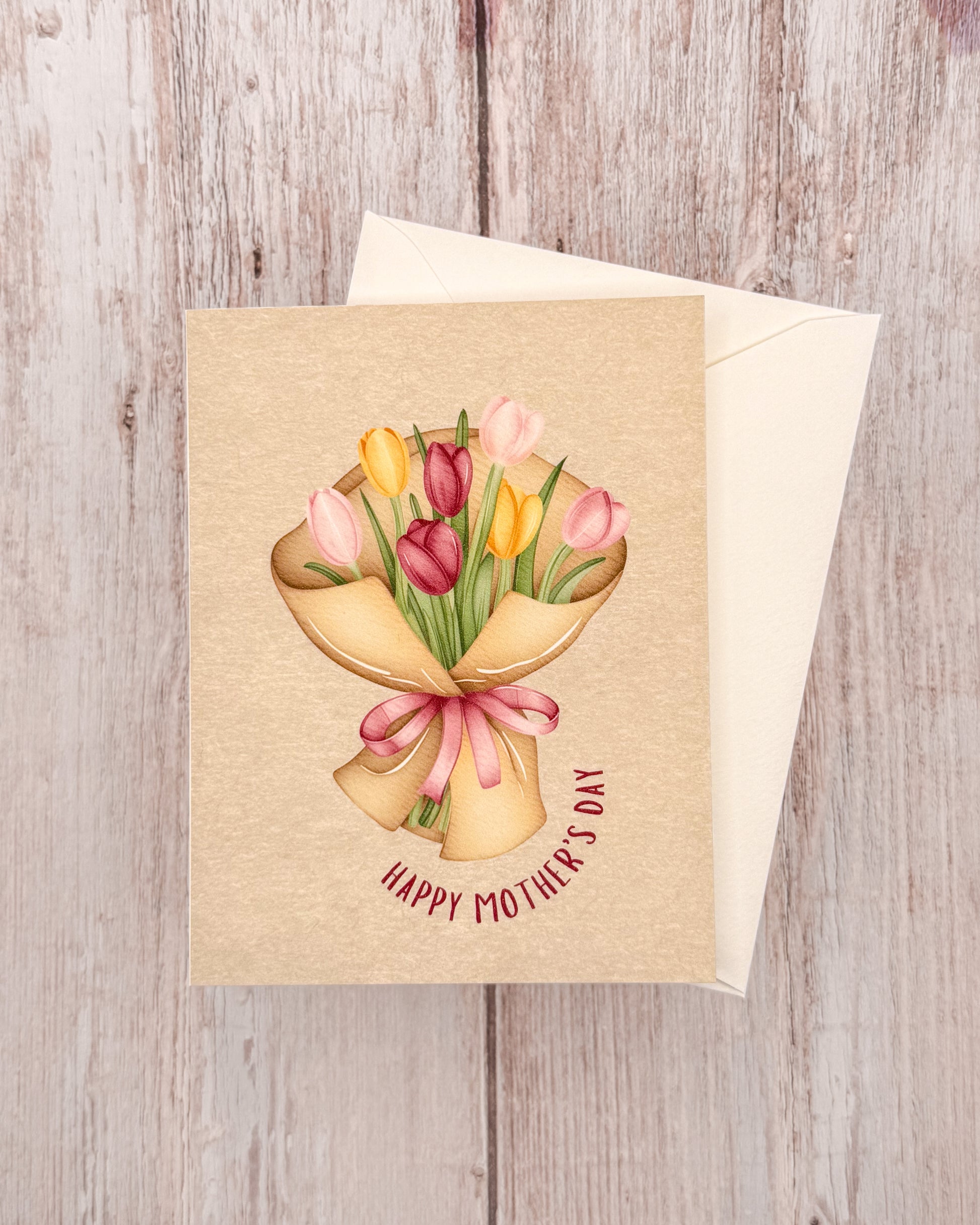 Greeting card with a illustration of tulips and 'Happy Mother's Day' text on a wooden surface.
