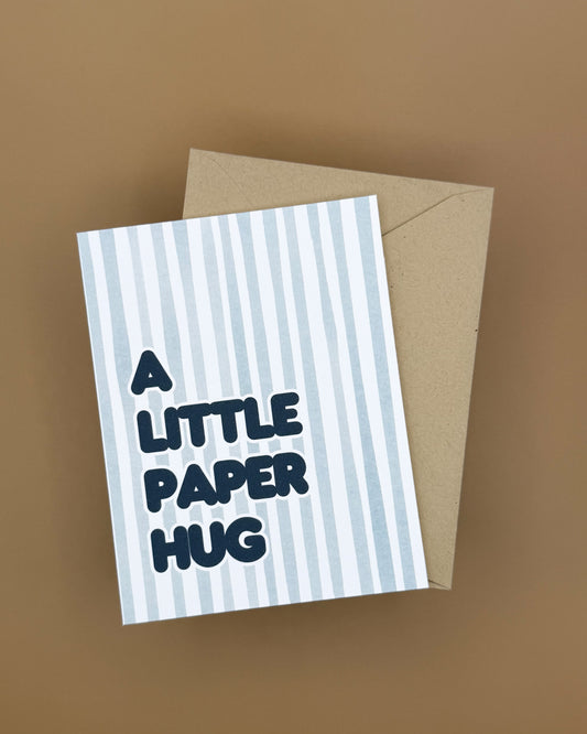 Greeting card with 'A Little Paper Hug' text on a striped design with a brown envelope.