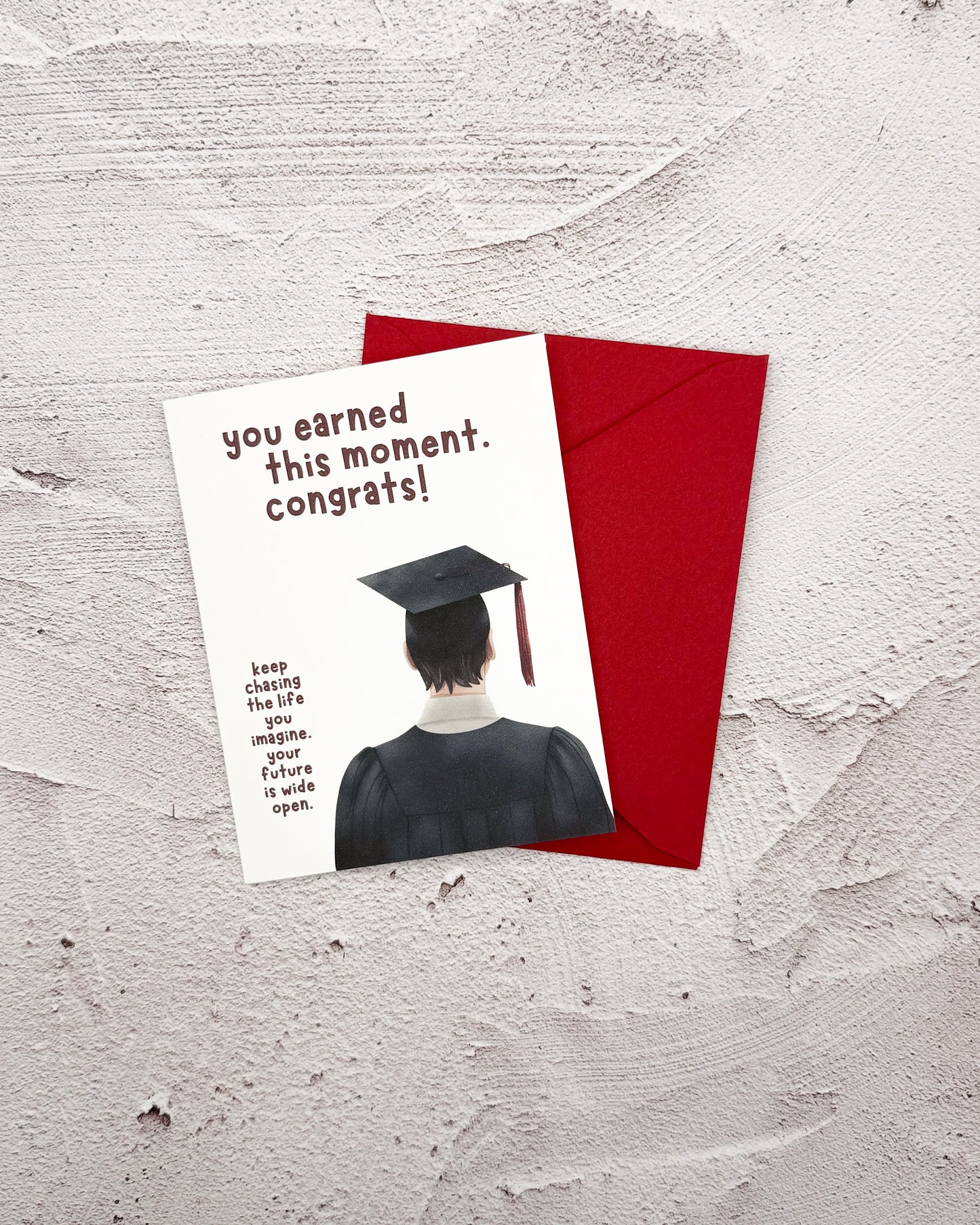 Graduation-themed card with a red envelope on a textured surface