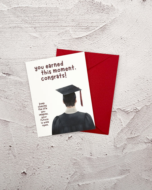 Graduation-themed card with a red envelope on a textured surface