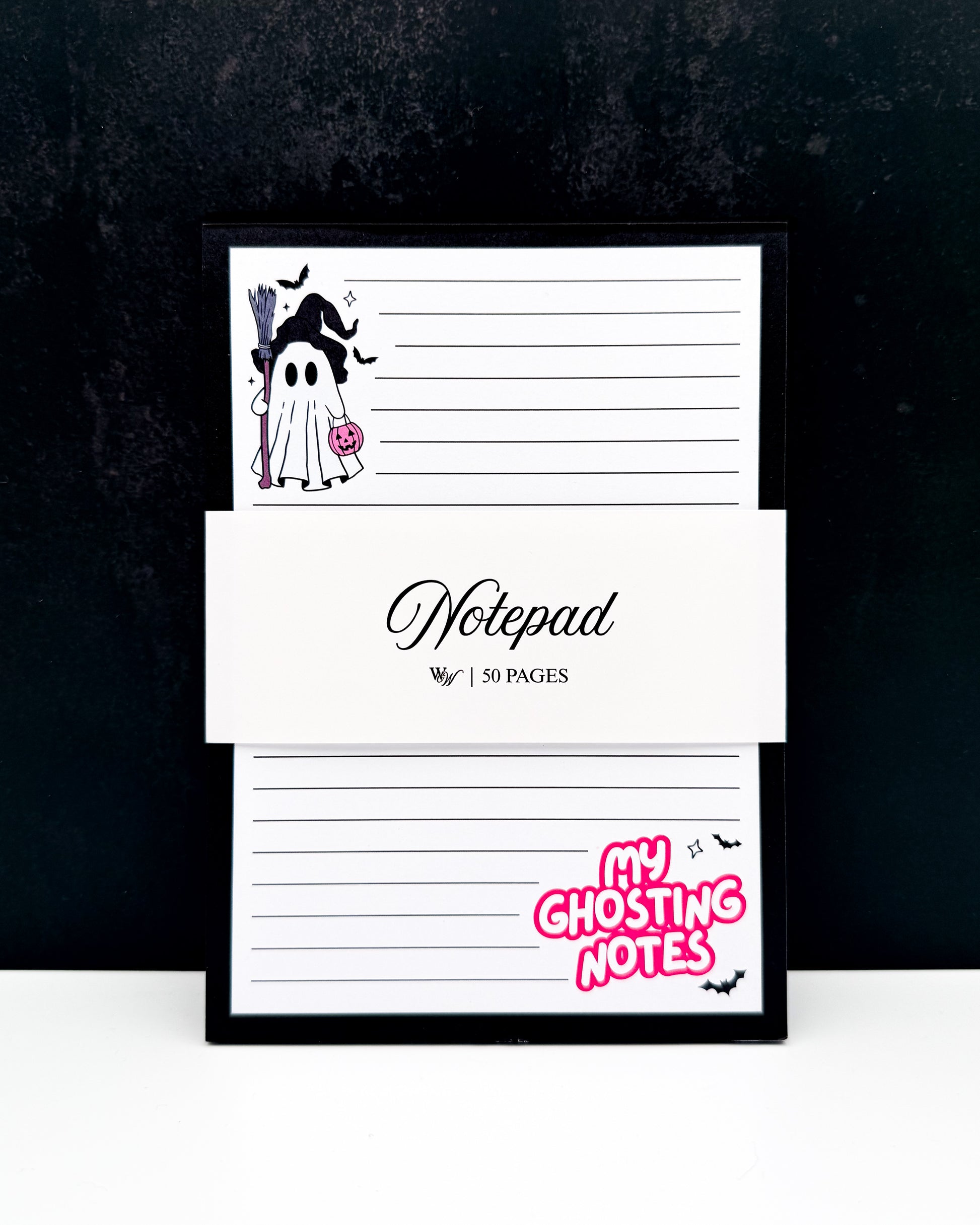 A framed notepad with a black frame, featuring a ghost illustration, lined writing pages, and a white paper band across the middle that reads 'Notepad' and '50 PAGES'. The bottom right corner has pink text reading 'MY GHOSTING NOTES' with small black bats.