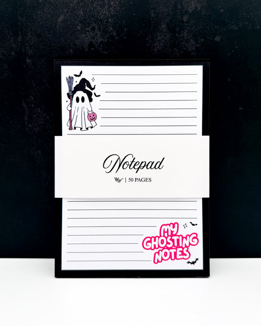 A framed notepad with a black frame, featuring a ghost illustration, lined writing pages, and a white paper band across the middle that reads 'Notepad' and '50 PAGES'. The bottom right corner has pink text reading 'MY GHOSTING NOTES' with small black bats.