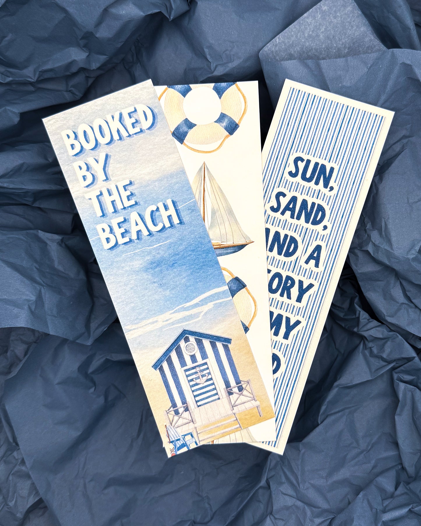 Three beach-themed bookmarks on a blue textured background