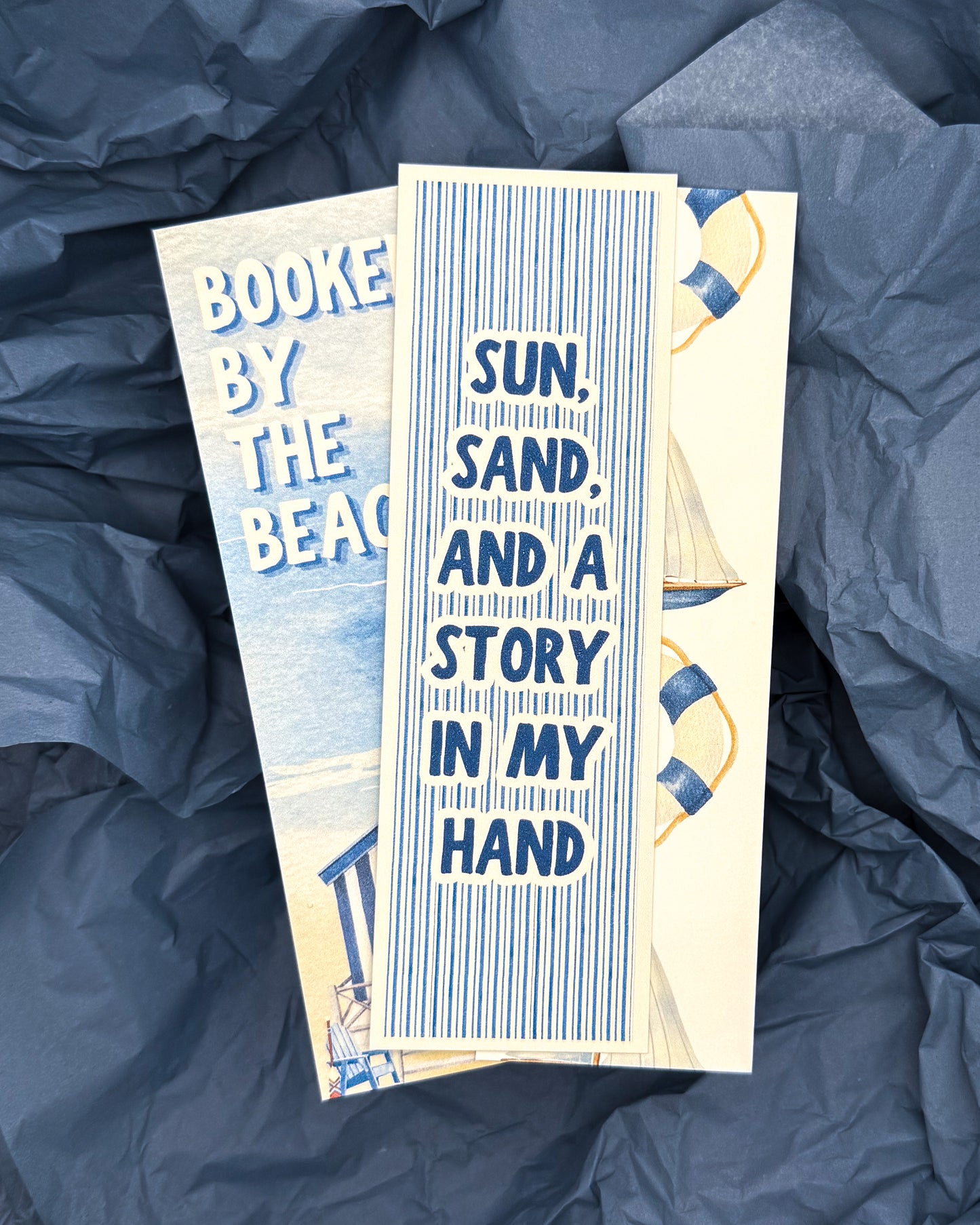 Two bookmarks with beach-themed designs on a blue crumpled paper background.