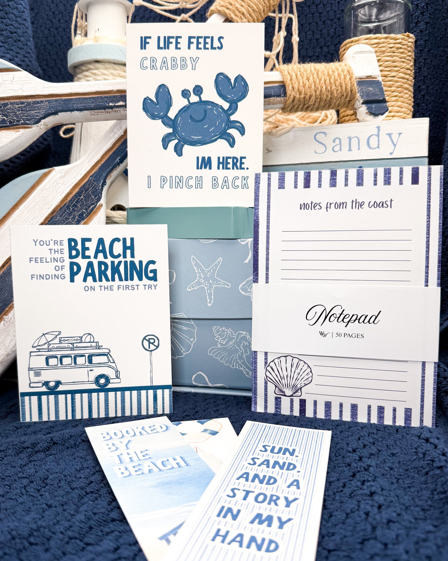 Collection of beach-themed stationery items including cards and notepads on a blue textured surface.