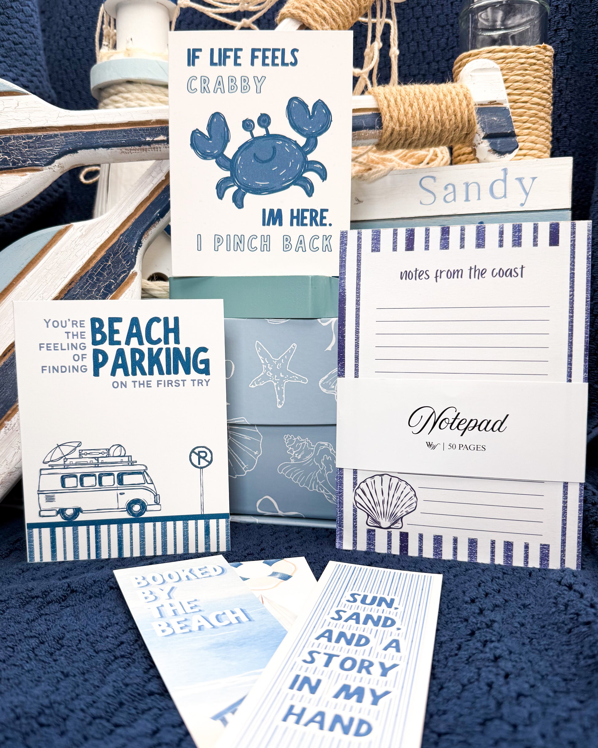 Collection of beach-themed stationery items including cards and notepads on a blue textured surface.