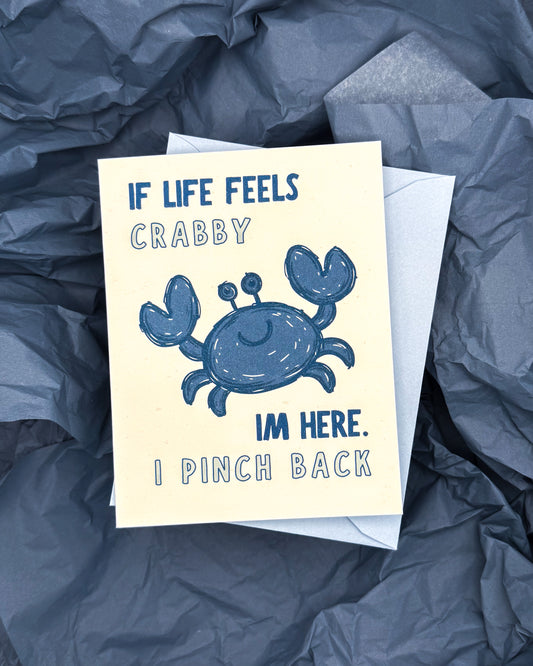 Card with a blue crab illustration and humorous text on a crumpled blue surface