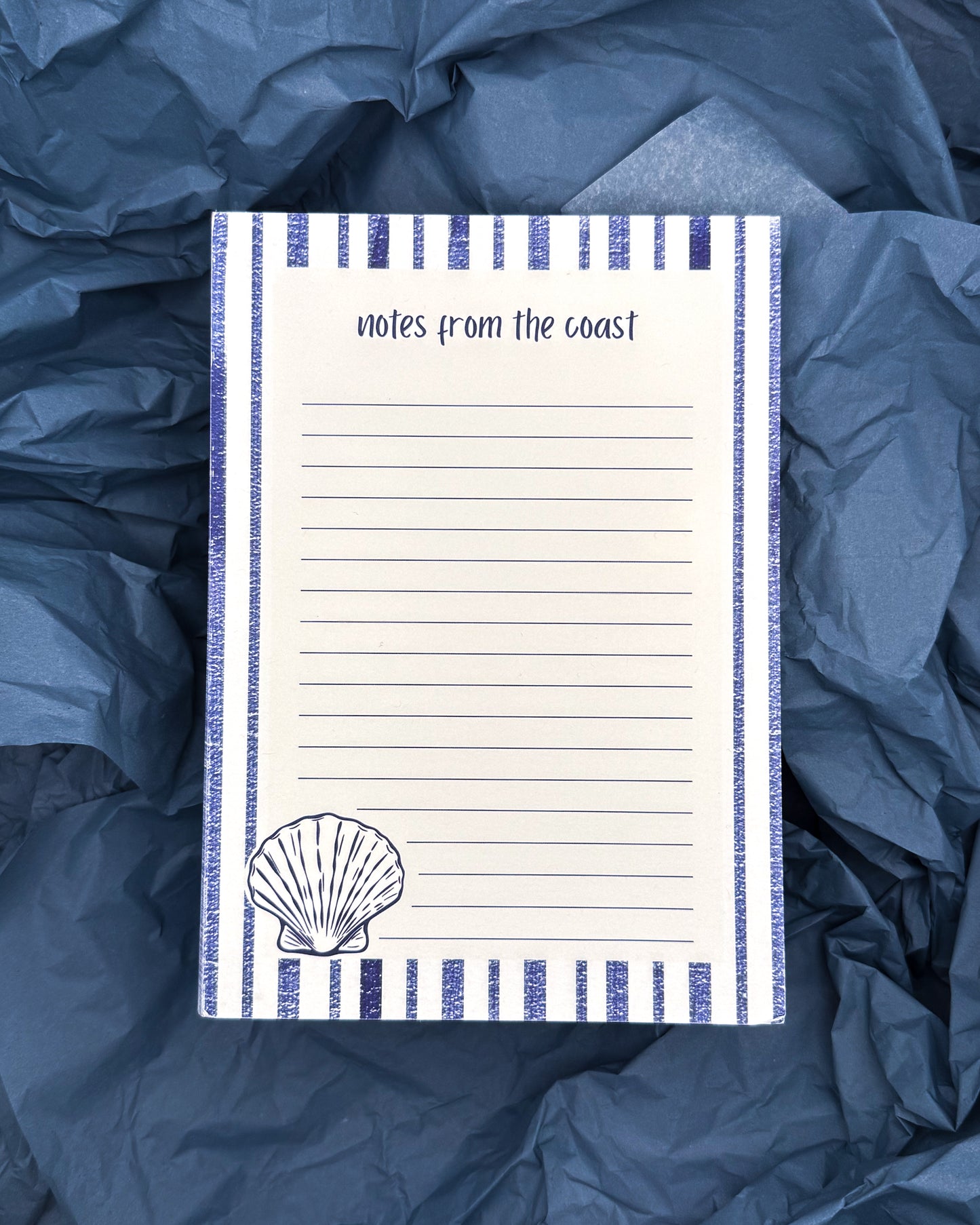 Notepad with 'notes from the coast' text and shell illustration on blue fabric background