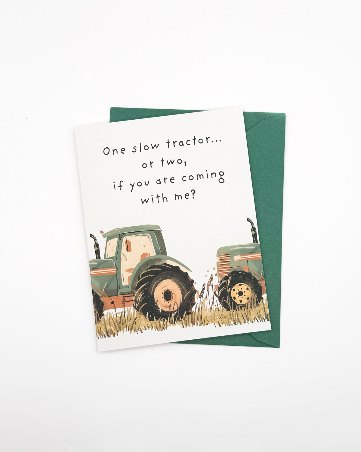 A white greeting card with a dark green envelope, featuring a watercolor-style illustration of two green tractors in a field and the text, 'One slow tractor.