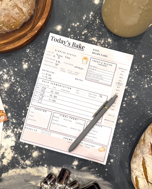Baking sheet with 'Today's Bake' form, ingredients, and a pen on a flour-dusted surface.