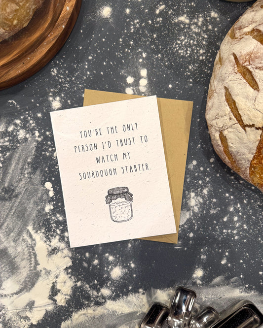 Greeting card with text and illustration on a flour-dusted surface with bread and baking tools.