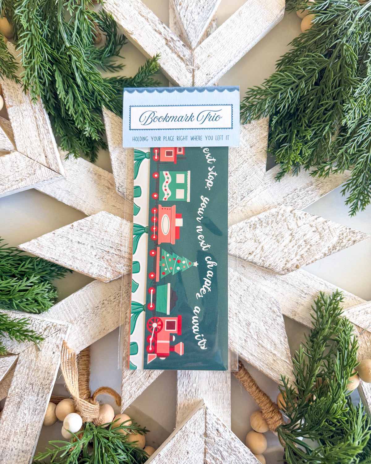 A packaged pencil with a Christmas-themed label reading 'Bookmark Chic' and 'Holding your plate right where you left it,' surrounded by rustic wooden star decorations and green pine branches.